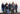 Group of seven people wearing matching navy blue hoodies in front of a white garage door.